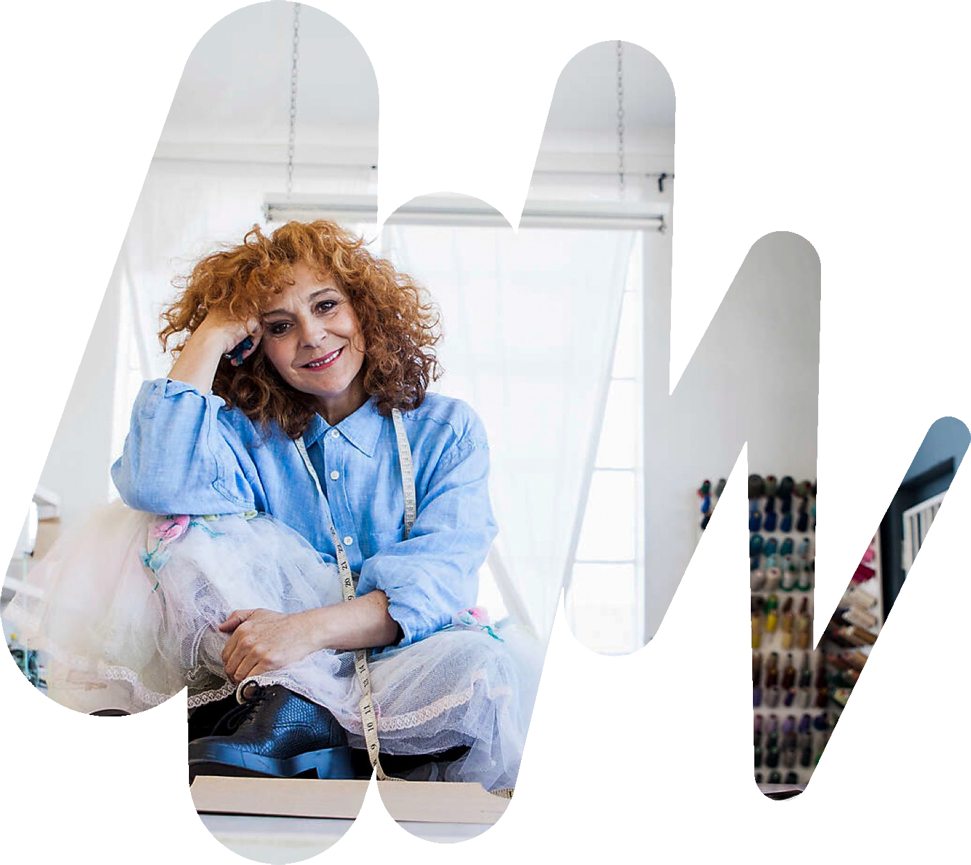 Eine Frau mit einem Maßband um den Hals lächelt in die Kamera. Um sie herum liegen Stoffe