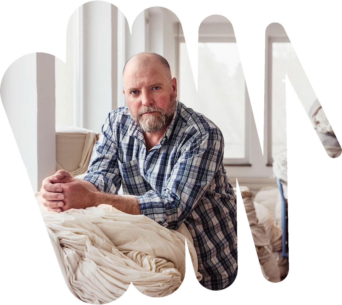 Ein mittelalter Mann blickt ernst in die Kamera. Er lehnt auf einem Stapel gewaschener Wäsche.