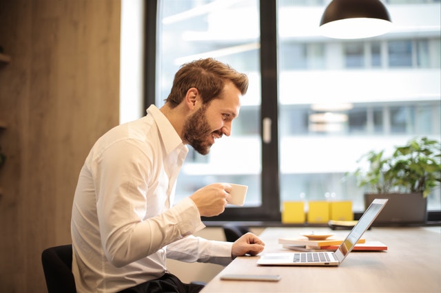 Man smiling at laptop, drinking coffee