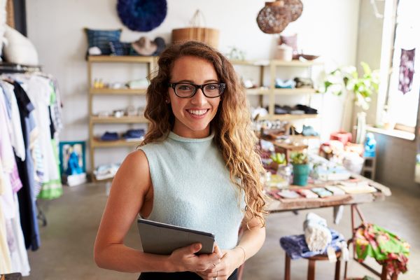 woman smiling, holding a tablet in a clothing store