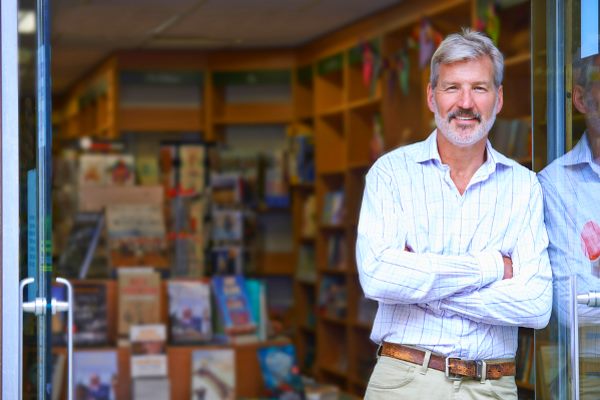 man leaning at door of a bookstore smiling