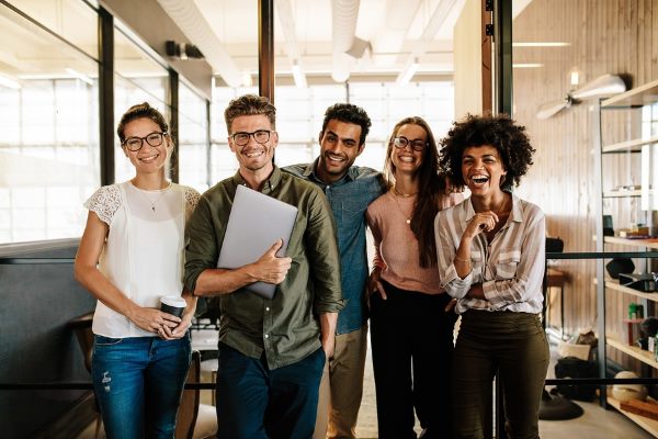 Write together a group of young people smiling while standing in the office